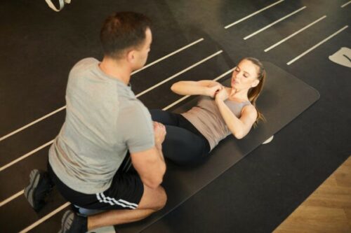 High angle view at muscular coach training young woman doing scrunches in gym, copy space